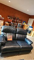 Frontal view of the navy blue LaZboy leather dual recliner sofa with the Leather Plus care kit box placed on the seat cushions.