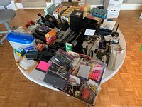 Overall view of the office supplies lot on a round table showing pens, staplers, hole punches, organizers, and office accessories