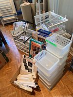 Multiple plastic storage bins stacked, black metal wine rack, folded white racks, and other organizers stacked on floor