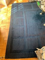 Flat navy blue area rug with geometric grid pattern in shades of blue placed on parquet floor, edges slightly rolled under.