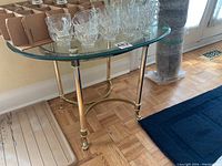 View of side table showing glass top and polished brass frame with some glass cups on top (not included)