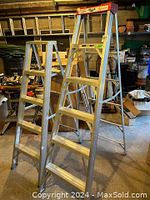 Two Lite brand aluminum step ladders, 6ft and 5ft, standing upright in a garage with some background clutter.