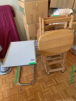 Wooden TV tables with caster wheels and foldable oval tops next to metal-frame tray table with patterned top
