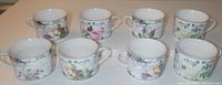 All eight coffee cups arranged in two rows on plain surface with their floral designs visible