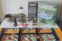 Wide shot showing all bird-themed items on a white surface including glass cloche, ceramic bowl, bird bath in box, bird figurines, and bird textile laid out below.
