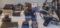 Overview photo showing multiple cameras and camera accessories including vintage and point-and-shoot models laid out on a table.