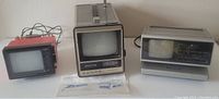 Three vintage portable televisions and a radio clock, showing front views of the items with wear and surface marks, all placed side by side on a white surface against a white background.