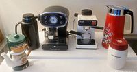 Full view of lot including two espresso machines, two thermal carafes, ceramic novelty coffee maker, and Starbucks items on white surface.