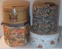 Four vintage round hat boxes stacked together showing various decorative designs.