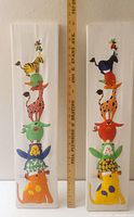 Front view of two tall vertical kids wall art pieces with colorful puffy fabric animals stacked, placed next to a 24-inch ruler for scale.