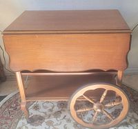 Front view of wooden tea cart showing the front panel, one large wheel, and the lower shelf.