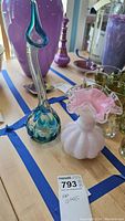 Two art glass vases on table with blue tape around them; one is tall with teal-blue detail, the other is pink with ruffled edge.
