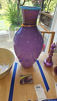 Front view of the tall purple art glass vase with teal rim and yellow adornments on a wooden table.