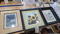 Three framed art prints side by side on a table among other items.