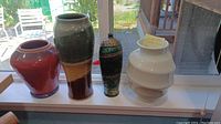 Four pottery vases, different shapes and colors, displayed on a windowsill.