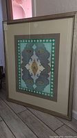 Framed signed art carpet titled Eastera by Lora Carson showing full artwork and frame.