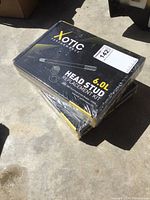 Two sealed black and yellow Xotic Performance 6.0L head stud kits on concrete floor