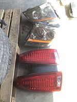 Four automotive lights on a concrete floor including two Cadillac CTS headlights and two taillights placed near a tire and wood pallet.