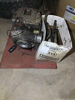 Side view of Garrett turbocharger unit next to white box containing additional parts such as hoses and metal rods.