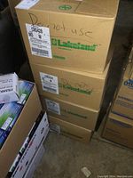 Four stacked cardboard boxes labeled 'Lakeland' with size markings for disposable coveralls