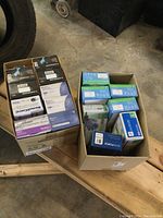 Two boxes showing multiple smaller boxes of vinyl and nitrile exam gloves in various brands and sizes.