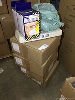Photo showing stacked boxes containing Clear Choice foam face shields, with North brand N95 respirator boxes on top and a plastic bag of boot covers visible.