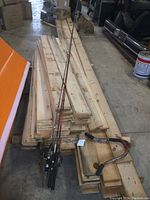 Three fishing poles with attached reels and an ice fishing pole with foldable metal stand placed on stacked wooden boards in a workshop or storage area.