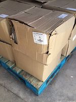 Damaged cardboard cases stacked on a blue pallet showing condition of packaging.