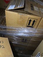 Closed cardboard shipping cases wrapped in plastic, marked with handling arrows and labels.