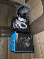 Two pairs of gaming headphones and one Logitech Driving Force Shifter box on leather seats, packaged and new.