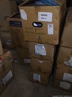 Four stacked cardboard boxes containing the isolation gowns, one box open at top, handwritten label mentions 'covers plus respirators'