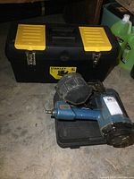 Stanley plastic toolbox with yellow latches, two blue pneumatic air nailers, and black Mastercraft case visible on the floor.
