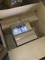 Overhead view of an open cardboard case showing several smaller retail boxes inside; one box opened showing multiple N95 respirators in sealed plastic packaging with blue and yellow markings.