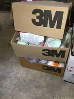 Three sealed cardboard boxes stacked containing new respirators, two of which bear the 3M logo prominently.