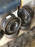 Stack of 4 black steel wheels showing front and side, with visible surface wear and minor rust spots.
