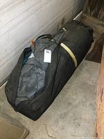 Black carry bag containing folded gray and blue tent fabric with attached pole visible inside.