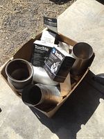Box containing multiple new truck exhaust parts including stainless steel exhaust pipe sections, flexible pipes, and boxed TorcTite exhaust clamps.