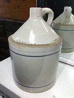 Front view of antique stoneware jug showing tapered conical top, finger handle, and blue stripe decoration.