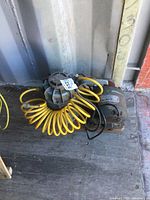Side view of electric air compressor unit with attached yellow coiled hose and power cord on wooden floor