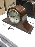 Full view of the antique wooden mantel clock with rounded top and key placed in front on a white surface.