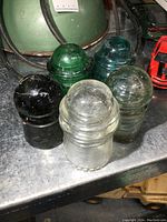 View of all five glass insulators showing varying shades from clear to dark green and black.