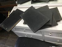 Seven black covered antique ledger books stacked and spread across a table, showing slightly textured covers with metal eyelets binding the spines.