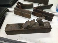 Overview of three wooden hand planes showing the largest plane in the foreground with a rounded handle and two smaller planes behind it showing names stamped on ends.