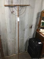 Full view of the antique wooden rake standing upright against a wall, showing the full length including handle and rake head.