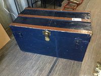 Front view of dark blue antique trunk with metal latch and brown wooden trim