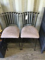 Front view showing pair of bar stools with metal slatted backs and fabric seats, placed on wood floor against wall.