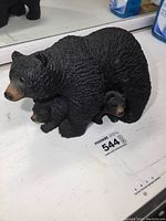 Front angled view of black bear sculpture with two cub cubs beneath the mother bear, showing texture in fur and overall shape.