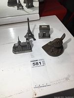 Overview photo of the cast iron bird doorstop and three Paris souvenir miniatures on a white surface with a mirror behind reflecting the items.