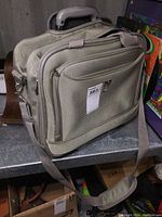 Gray Delsey carry-on travel bag showing front zippered compartments, adjustable shoulder strap, and pull-out handle.