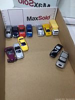 Photo showing 12 die cast cars and trucks arranged inside a box for scale and display.